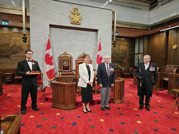 찰스 3세 대관식 메달 수여식을 앞두고, 앙드레 페텔르 옹과 연아 마틴 의원 등 관계자들이 상원 회의장 중앙 연단 앞에 엄숙하게 정렬해 있다.